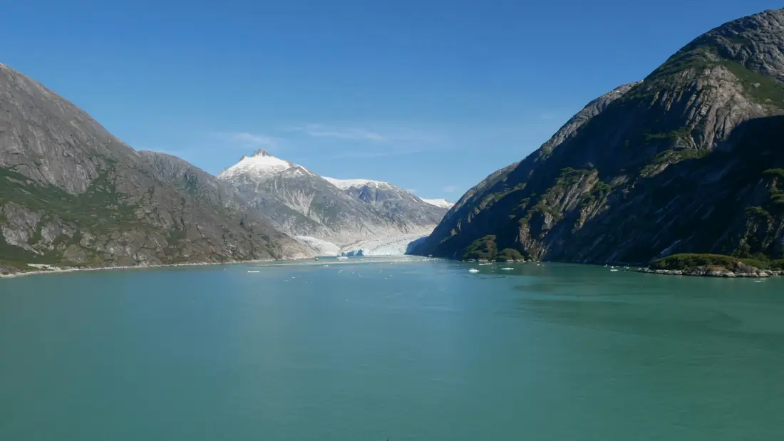 A calm turquoise fjord between granite mountains, with a glacier and snowy peak in the distance