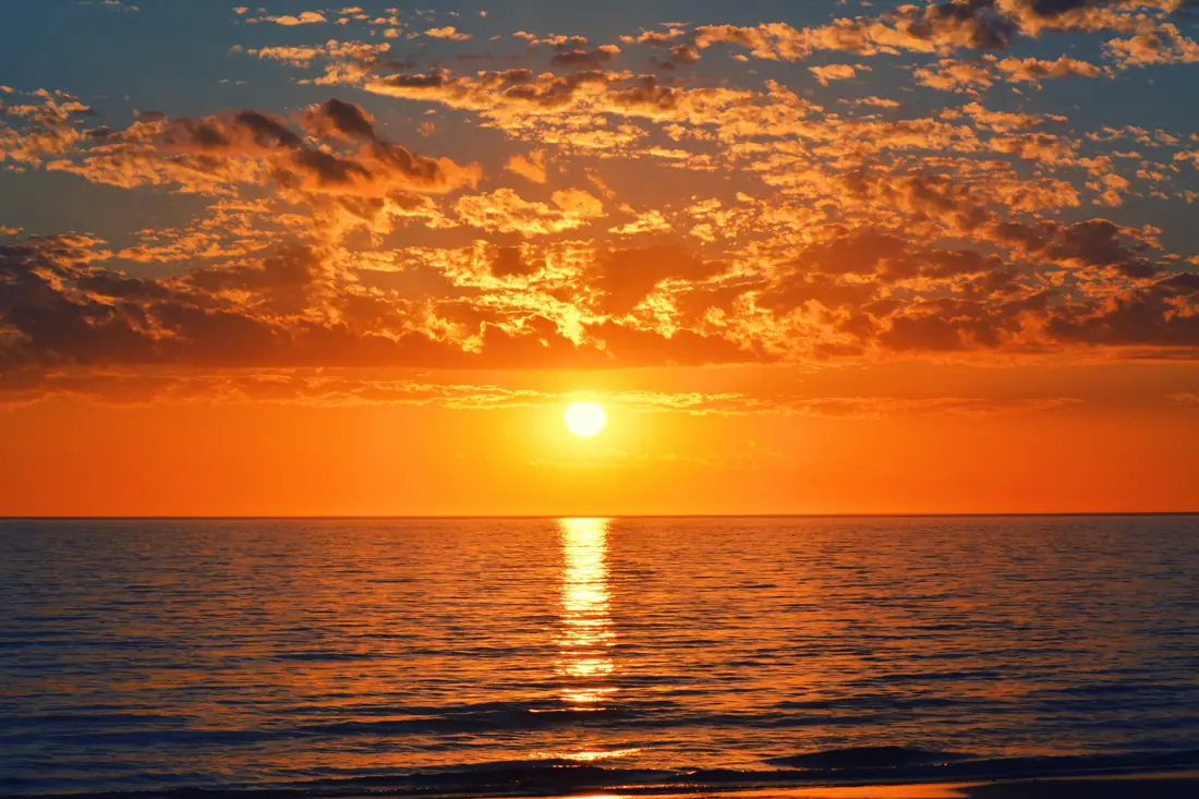 Low sun over a calm ocean with orange clouds